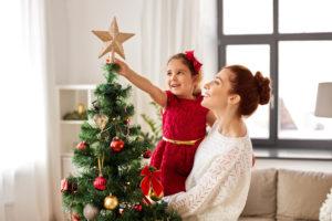Woman co-parent holding little girl up to put star on Christmas tree.